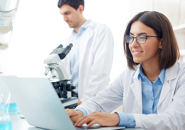 Two scientists in lab, one using a laptop