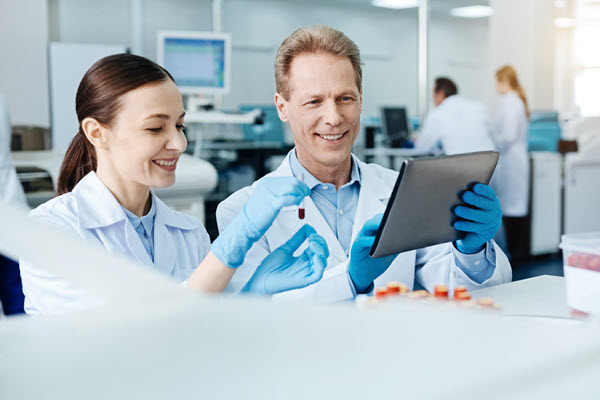 Two lab people looking at a tablet with sample vial in hand.