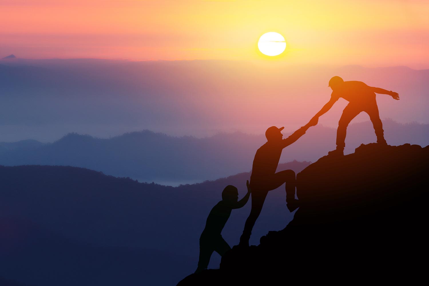 Silhouette of three men helping each other climb a mountain