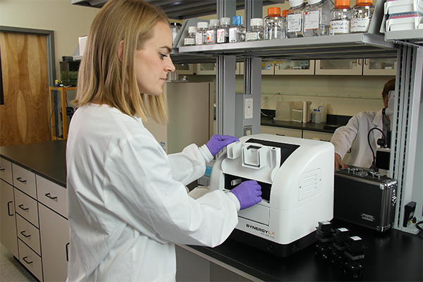 Scientist with purple gloves working on the BioTek Synergy Multi-Mode Plate Reader